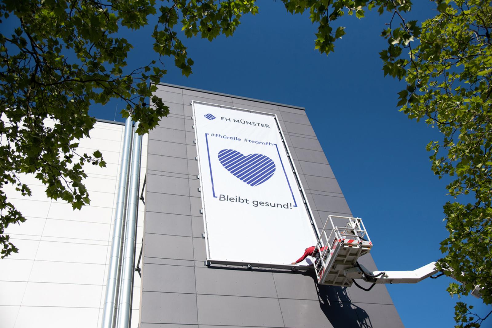 „Bleibt gesund!“ ist die Botschaft der beiden Banner. Eins davon hängt am Fachhochschulzentrum (FHZ). (Foto: FH Münster/Katharina Kipp) 
