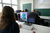 Blick über die Schulter auf einen Bildschirm. Rechts wird eine Programmierumgebung dargestellt, links das Programm Minecraft, in dem im Vordergrund ein großer blauer Würfel dargestellt wird.